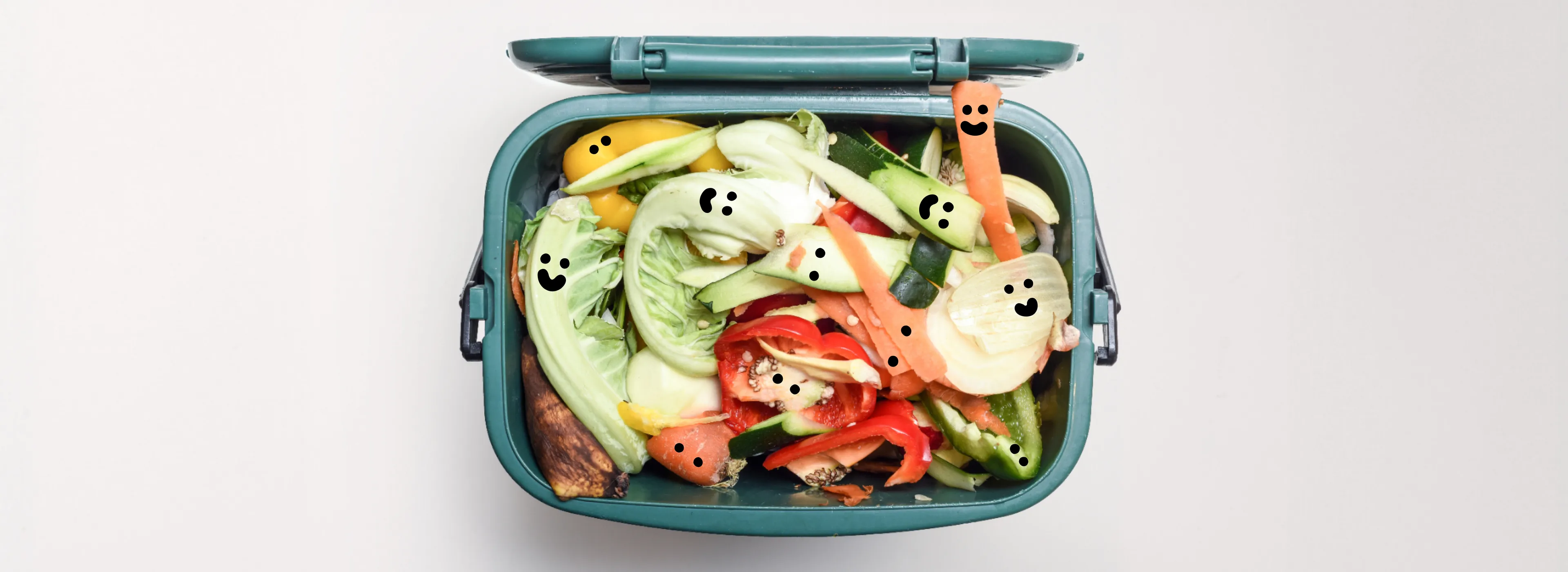 A teal compost container filled with vegetable scraps, each bearing a tiny smiling face